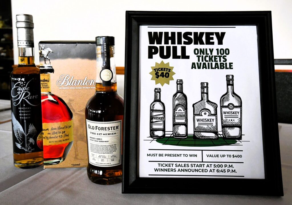 A promotional setup for a whiskey pull event featuring two bottles of whiskey, Eagle Rare and Old Forester, with a Blanton's box and a framed sign announcing the event details.