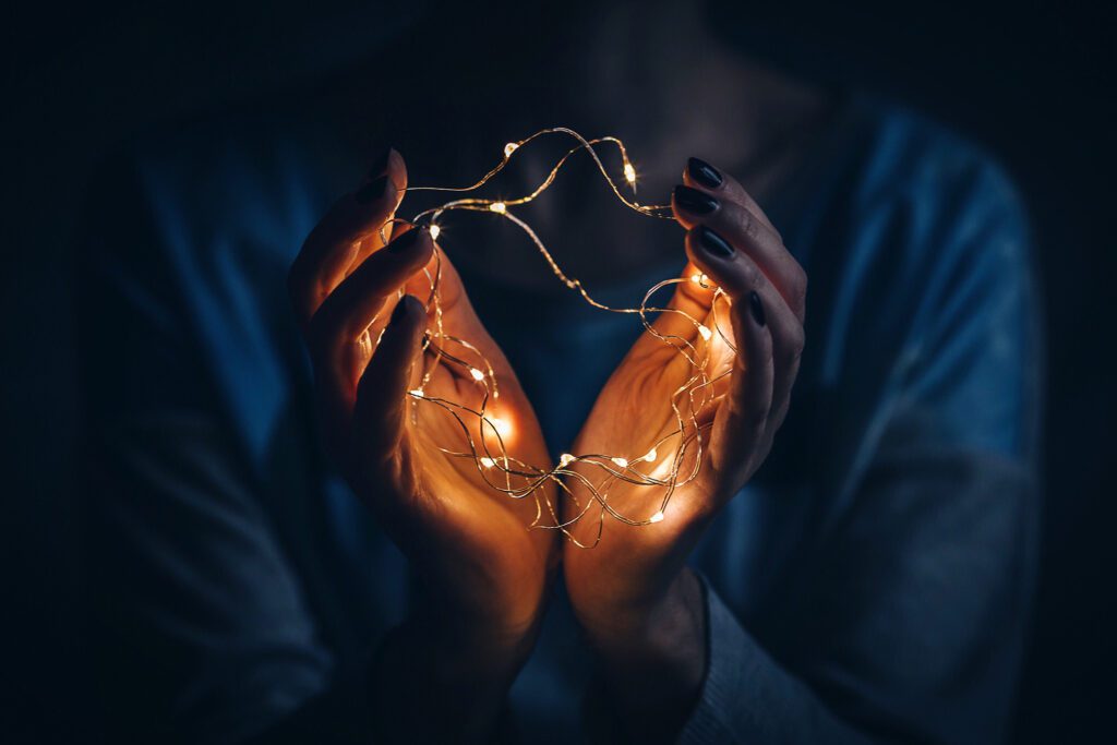 Hands gently holding glowing string lights in the dark, creating a warm and intimate atmosphere.