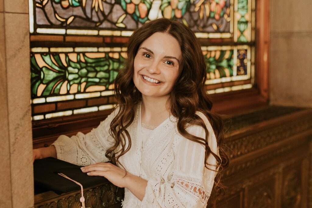 Skye Andre, Emmaus Homes Advocacy Intern, smiling in front of a colorful stained glass window.