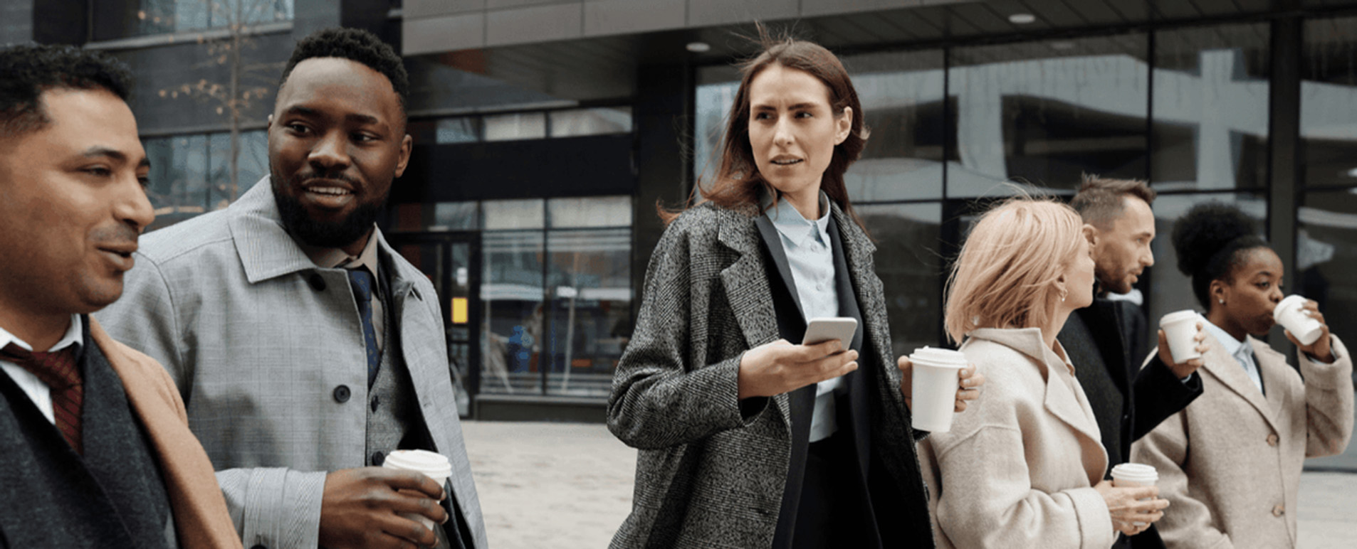 A group of professionals walking outdoors, holding coffee cups, and engaging in conversation.