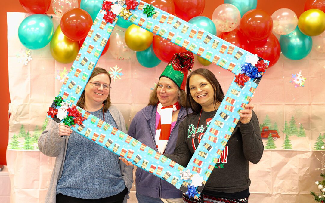 Emmaus employees at a festive Christmas party, smiling and holding a holiday-themed photo frame.