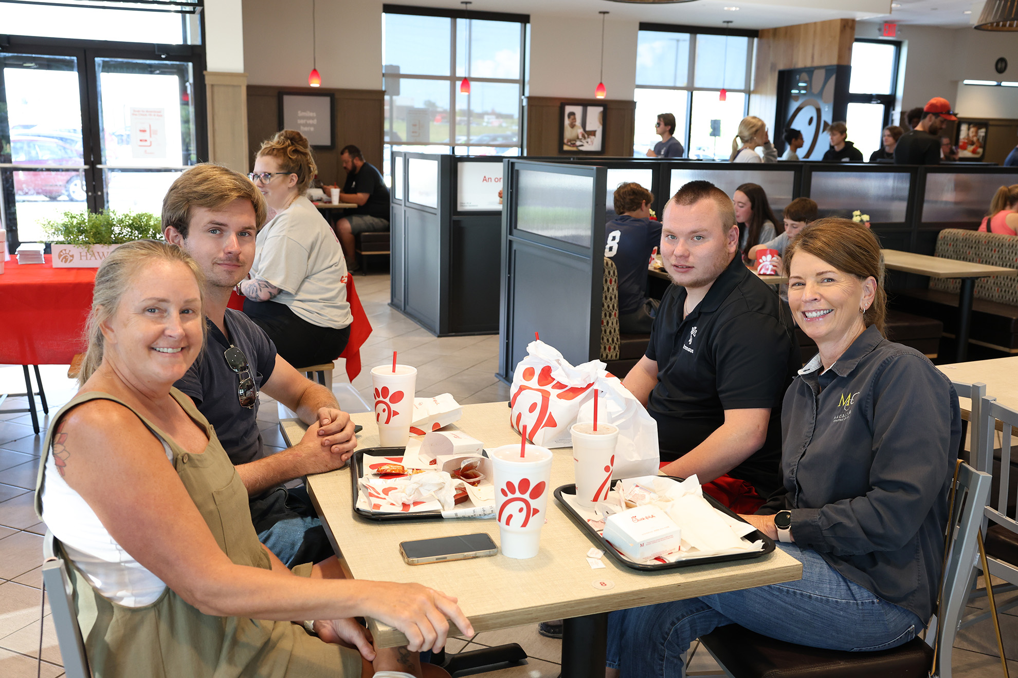 chick-fil-a A group of four people enjoying a meal at Chick-fil-A during Emmaus Night, smiling at the camera in a busy restaurant.