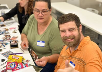 Man in an orange shirt gives a thumbs up while a woman next to him examines a printed photo.