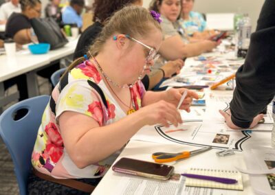 Woman in a floral shirt concentrates on her storyboard while seated at a long table with others.