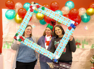 Emmaus employees at a festive Christmas party, smiling and holding a holiday-themed photo frame.