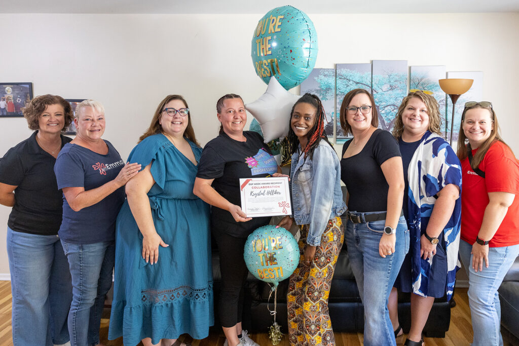 Emmaus team members celebrate a DSP award recipient, who holds a certificate and balloons, surrounded by smiling colleagues.