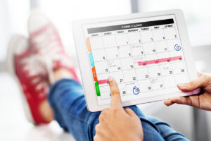 Person pointing at a digital calendar on a tablet while sitting back in casual shoes.