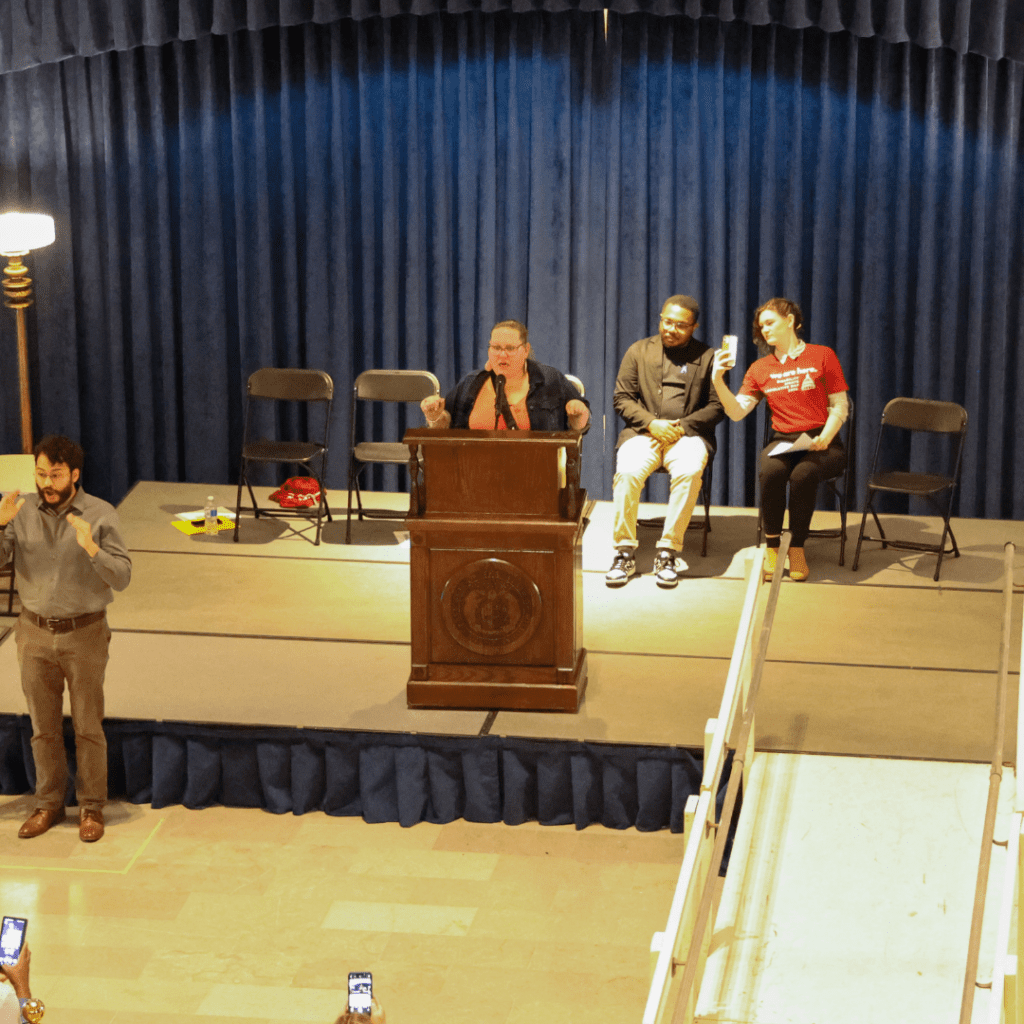 Susie Parker, an Emmaus Board member, is delivering a speech at the State Capitol during the DRLD Rally with audience members in view.