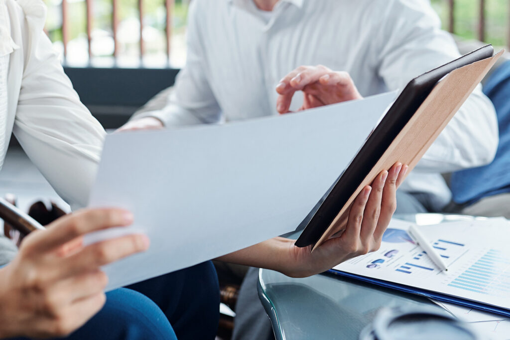 Two professionals reviewing a document and tablet with charts on a table.