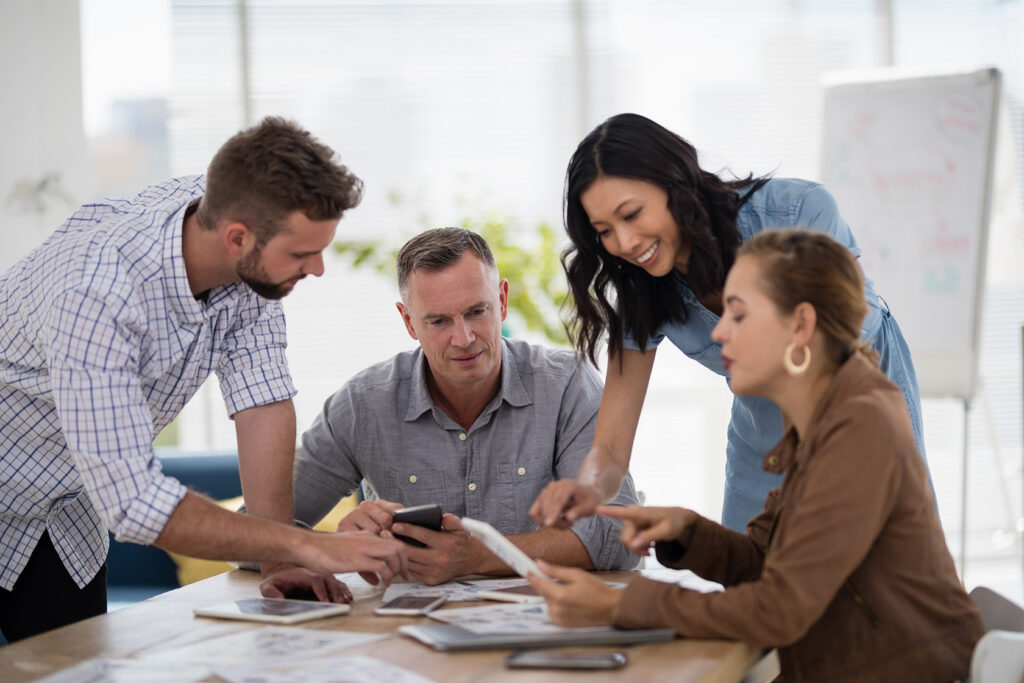 Four diverse professionals collaborating at a table with digital tablets and papers during a leadership discussion in a bright office setting.