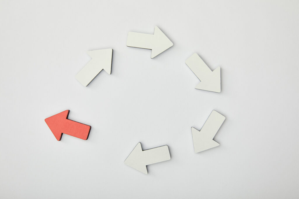 A circular arrangement of arrows, with five white arrows moving clockwise and one red arrow pointing counterclockwise, symbolizing breaking a repetitive cycle.